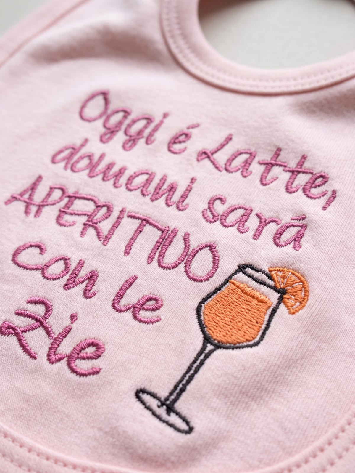 Dettaglio del ricamo sulla bavetta rosa con coppa e arancia